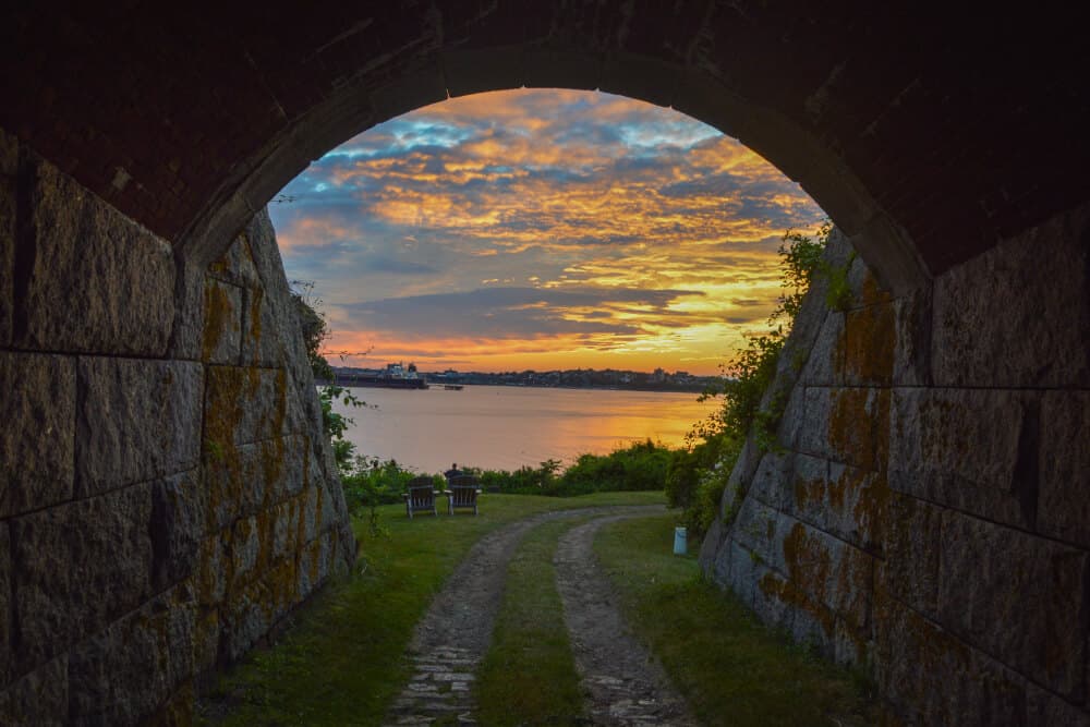 View of a sunset over a calm body of water framed by a stone archway.